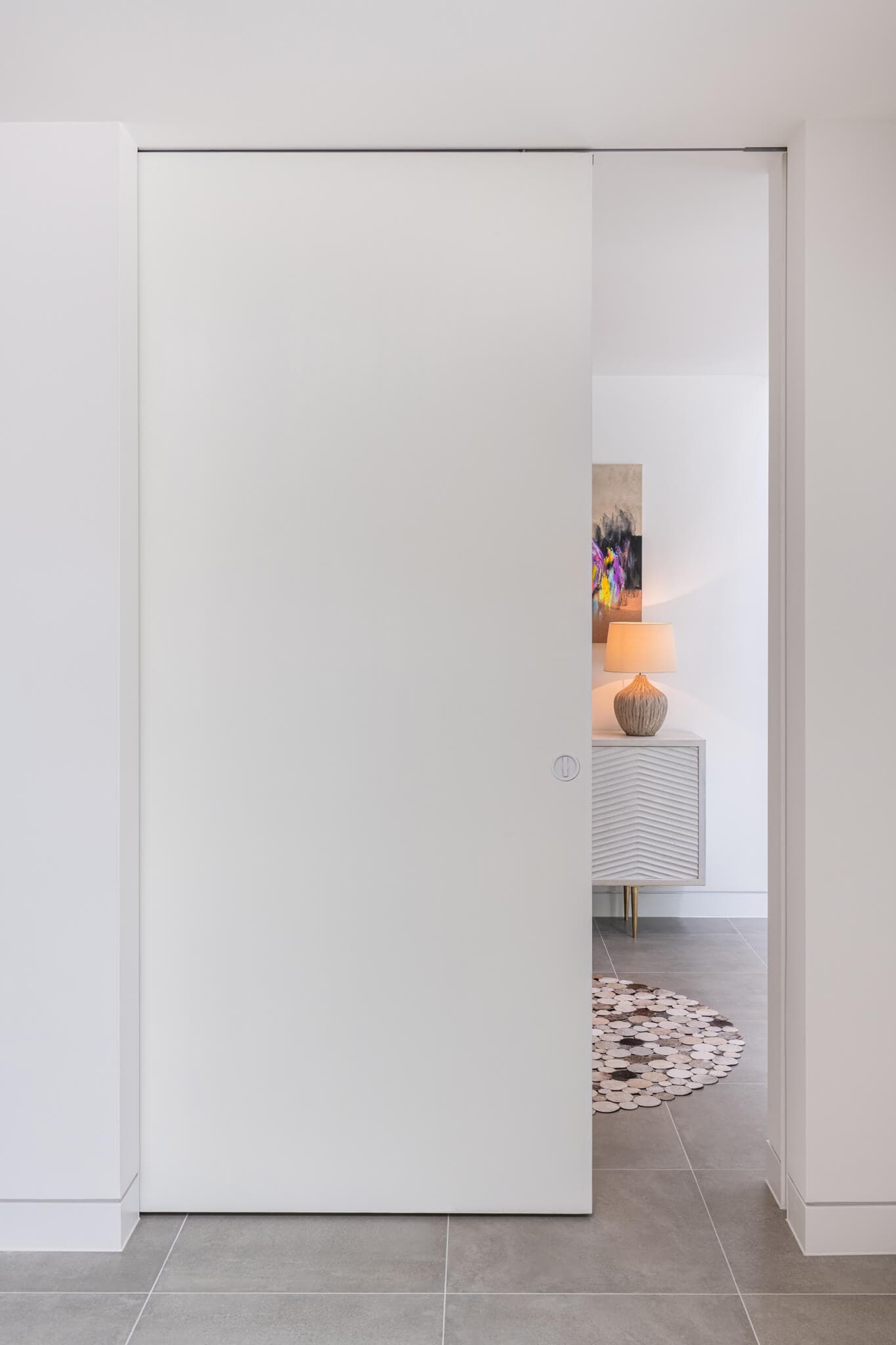 A modern interior with white walls and a white sliding pocket door partially open leading to a reception area.