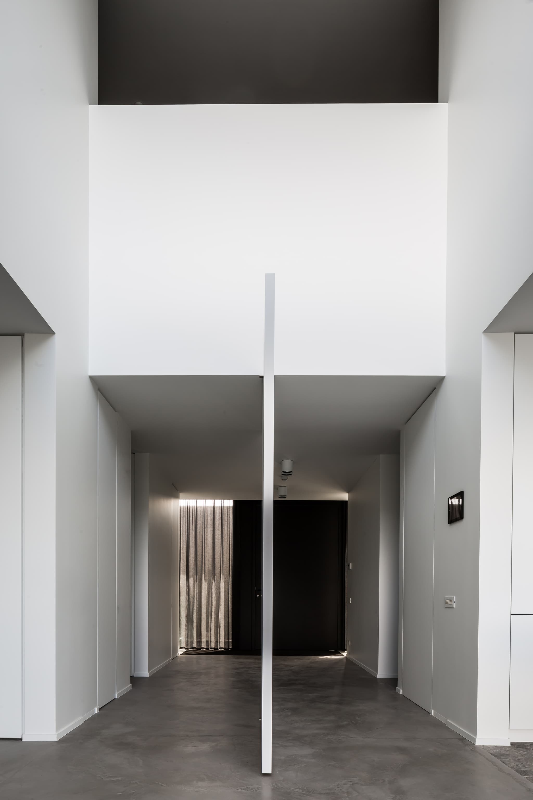 Side profile of a fully open pivoting flush door in a large space with concrete floors and white walls leading towards a dark coloured entrance door.