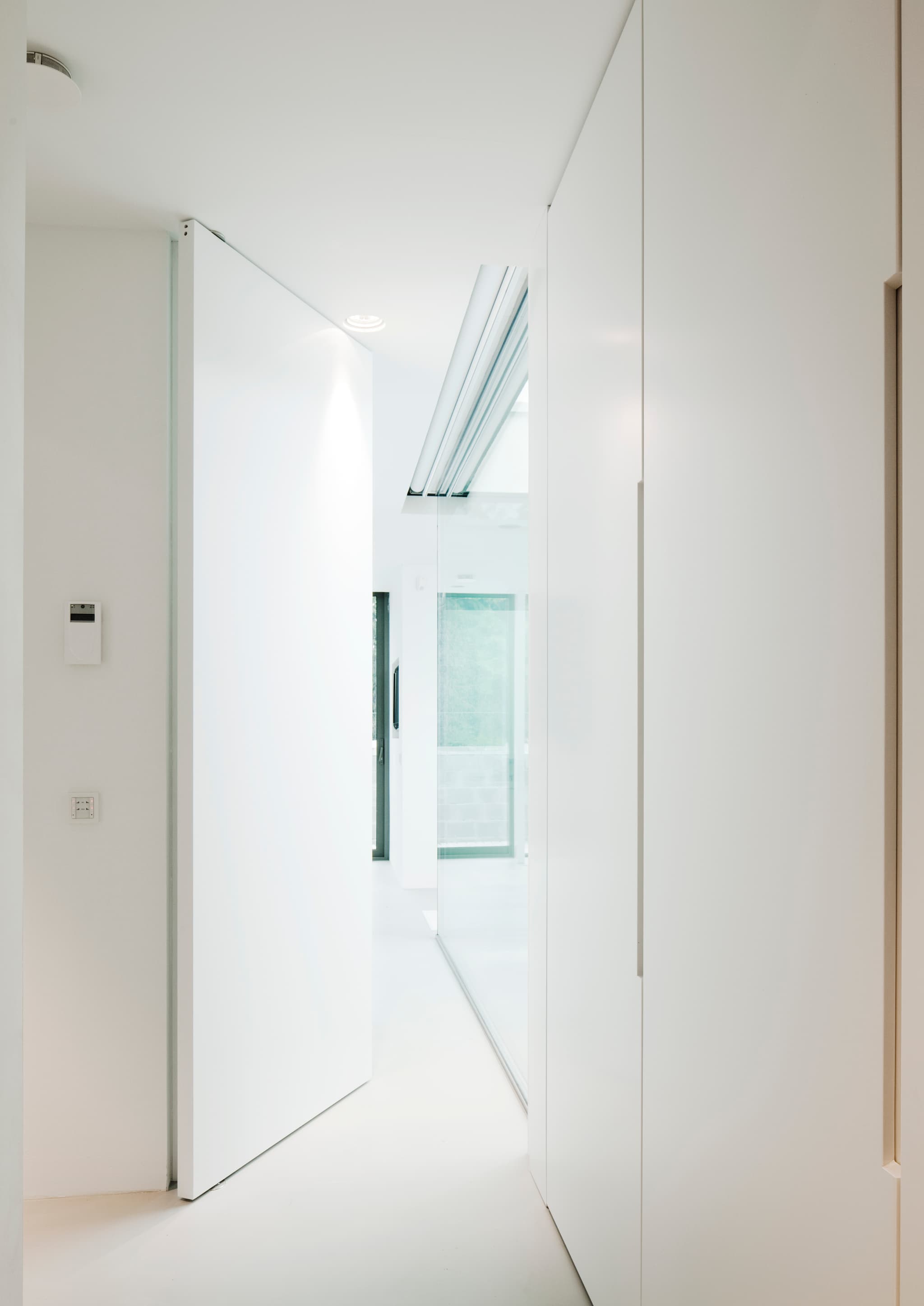 A large pivoting flush door slightly ajar leading into a corridor with full height glazing on the right hand side.