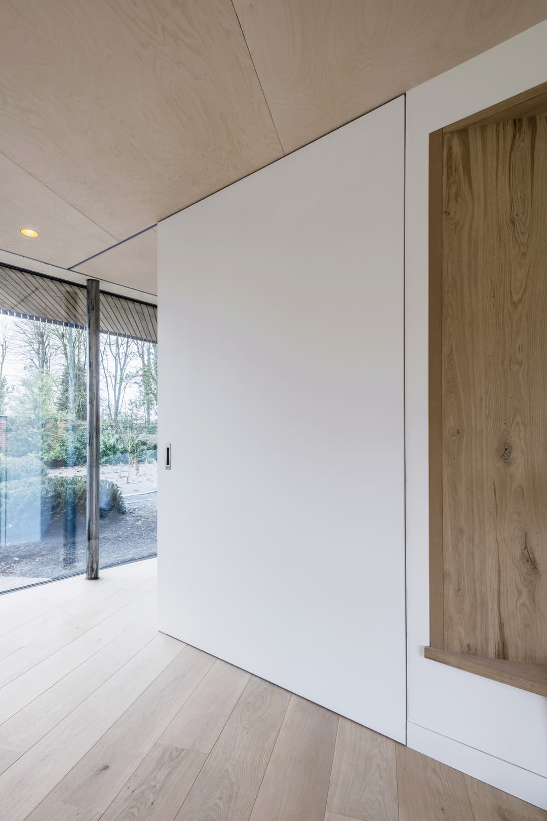A huge white sliding pocket door in a modern minimal interior with floor to ceiling glazing and wooden floor