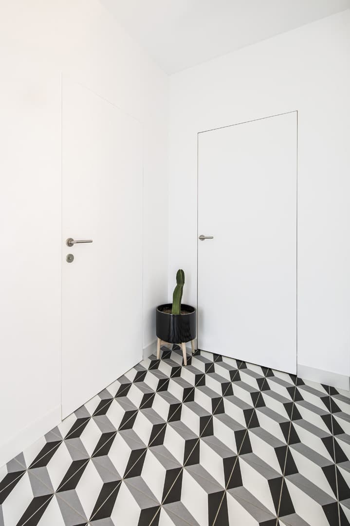 A black, grey and white tiled room with a plant in a black pot with two white invisible flush doors with silver lever handles.